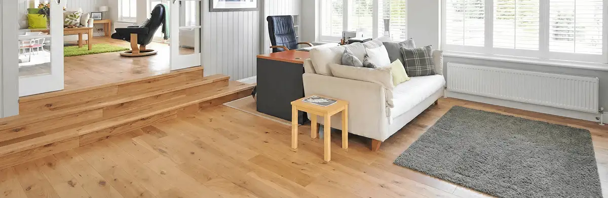 A modern living room with professionally installed laminate flooring, a beige sofa, a small side table, a gray rug, and large windows with white shutters in Kansas City, MO